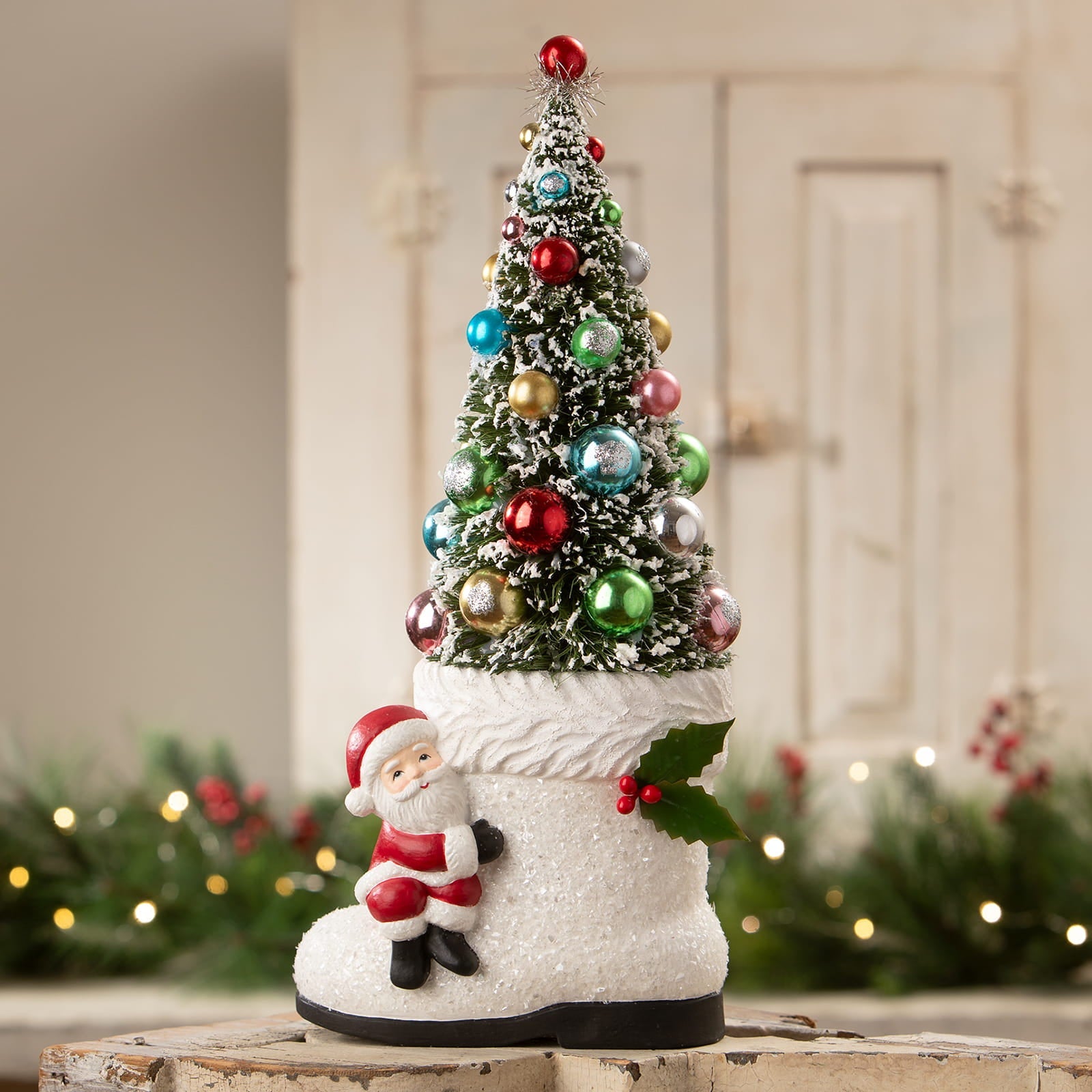 A festive bethany lowe design santa boot with tree featuring colorful ornaments and green holly leaves in white boot