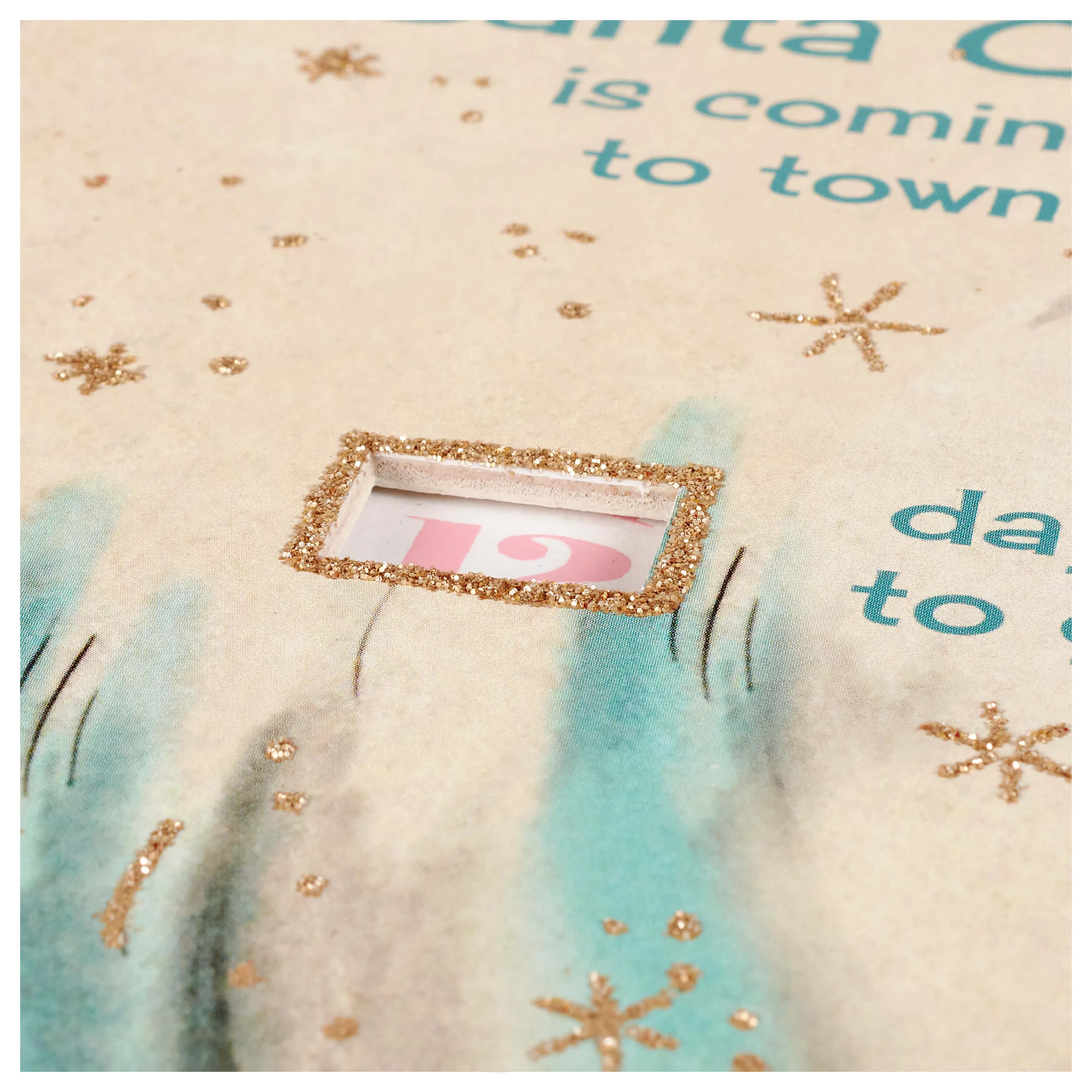 A pastel christmas countdown wheel with a glittery gold window on cream fabric featuring teal and gold stars and pink lettering