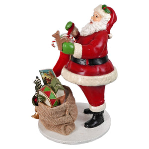 Santa filling the stocking figurine by bethany lowe designs red and white santa holding green toy beside burlap sack holiday items