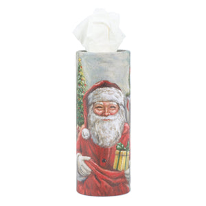 A cylindrical santa tissue box holder with a painted santa in red suit holding a gift next to a christmas tree for daily totes set