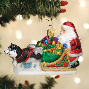 Glass santa’s dog sled ornament with black and white husky pulling red sleigh with colorful gifts and glittery green trim
