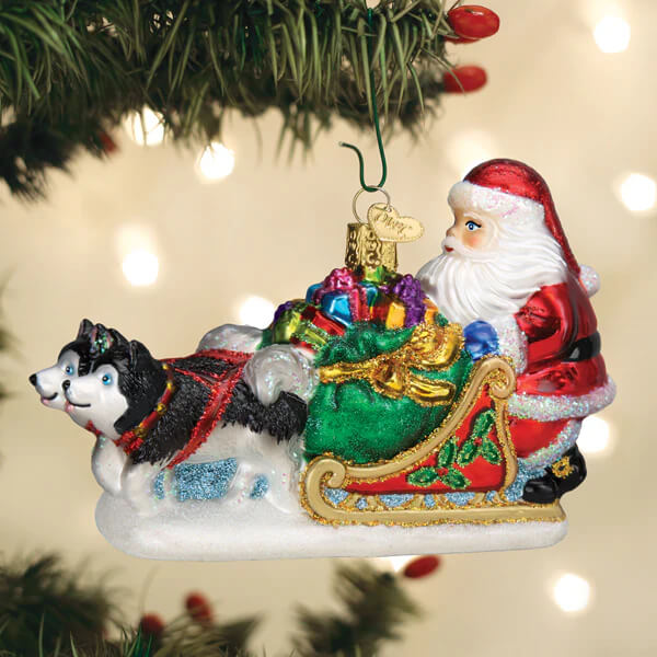 Glass santa’s dog sled ornament with black and white husky pulling red sleigh with colorful gifts and glittery green trim