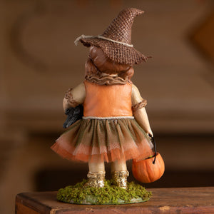 A charming scarecrow autumn figurine of a young witch in an orange dress with a brown woven hat and gold glitter boots