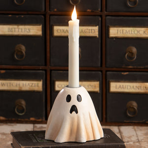A white ceramic scared ghost candlestick with black cutout eyes and mouth holding a lit taper candle perfect for halloween ghost figures decor
