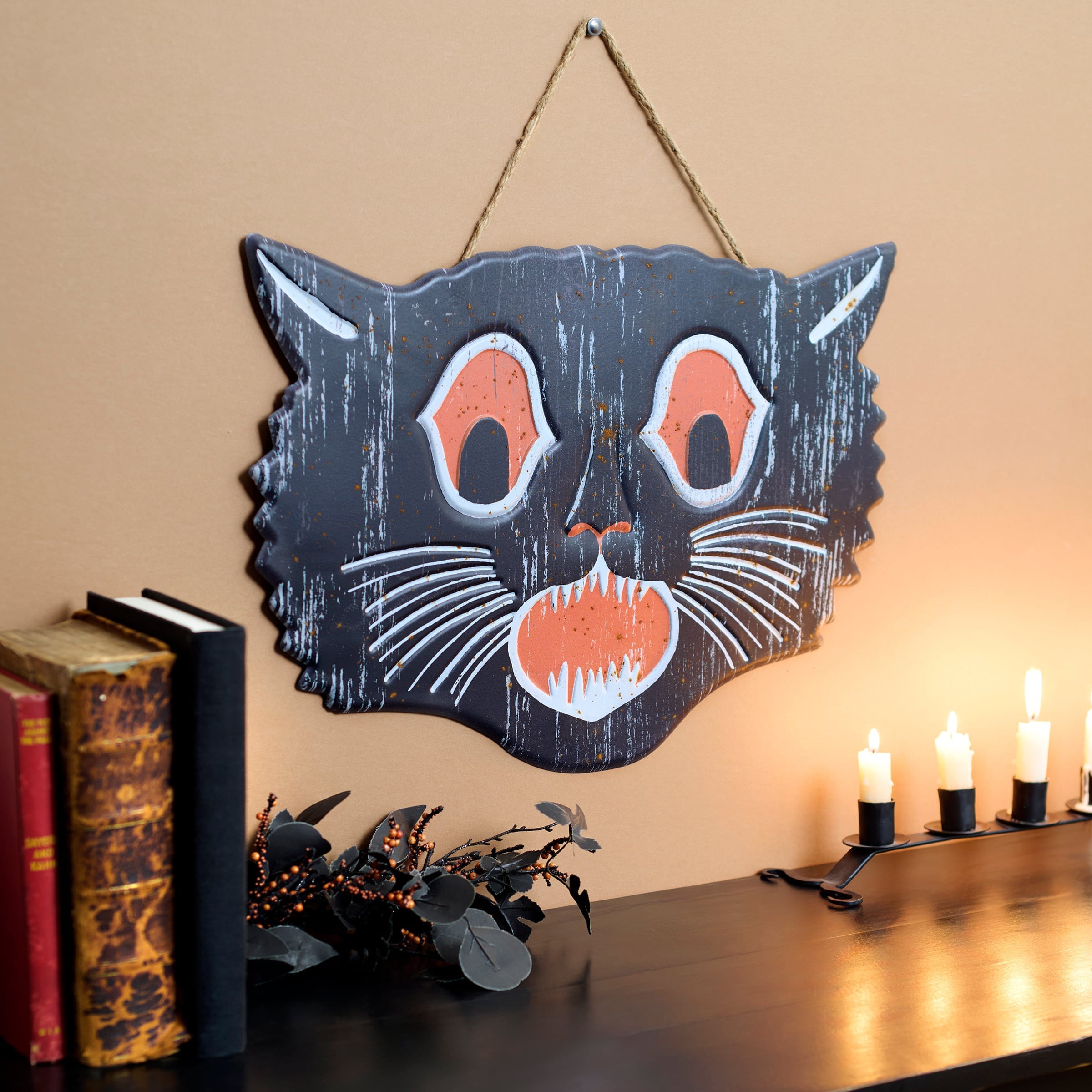 A rustic scary cat face wall hanging with orange eyes, white whiskers, and distressed black finish for cat face wall decor