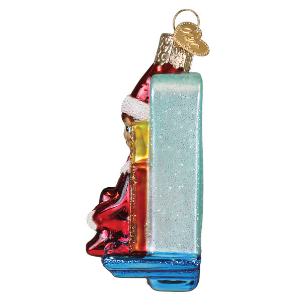 A festive glass christmas ornament featuring santa in red and white with a glittery blue book for scout elf storytime