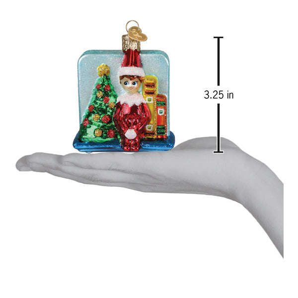 A festive red and white scout elf storytime christmas glass ornament with elf and gifts by a decorated tree