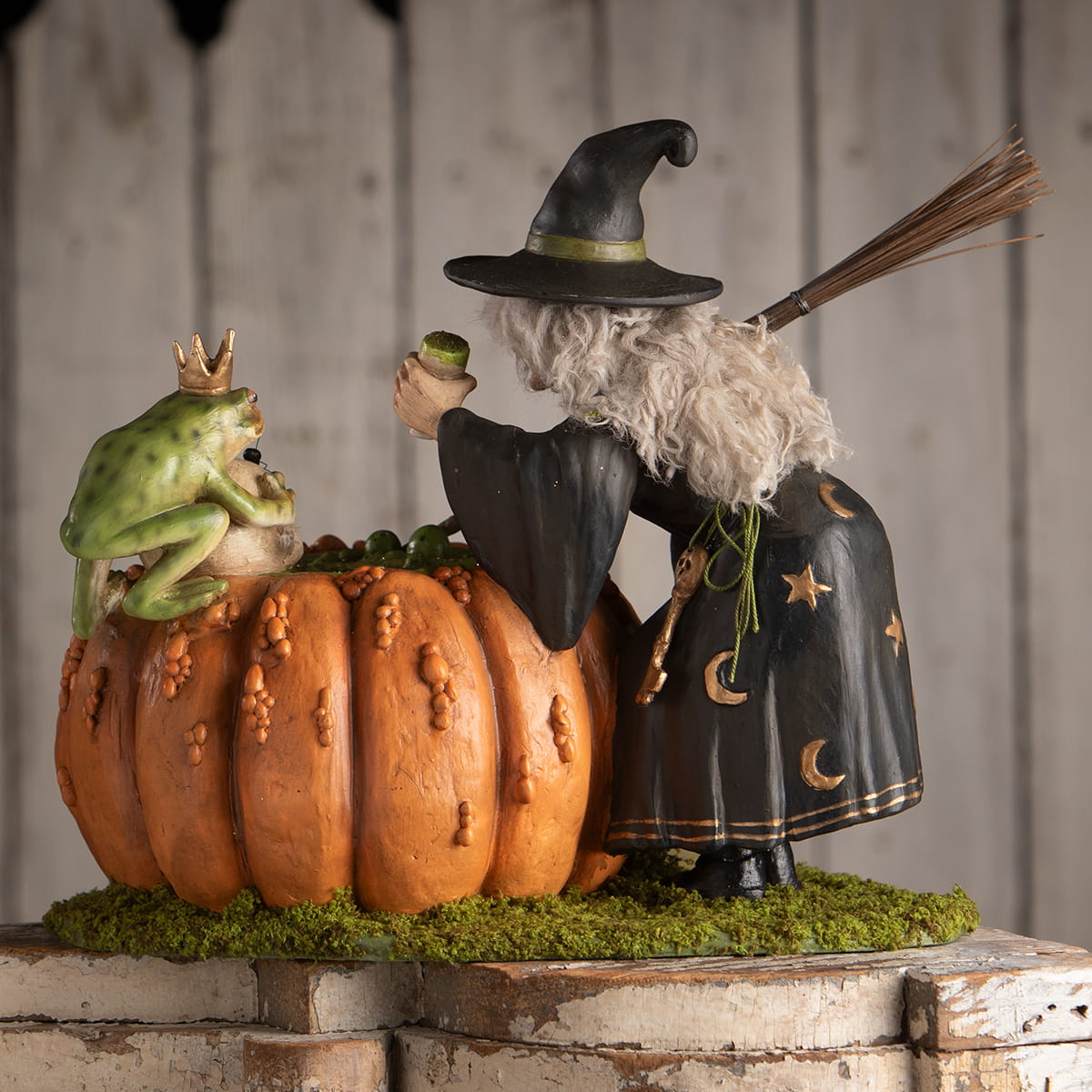 A whimsical halloween witches figurine of a black hat witch holding a green prince potion beside a pumpkin with a crowned frog