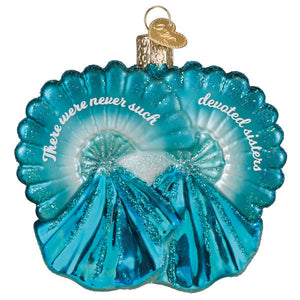 A translucent turquoise glass ornament shaped like overlapping seashells with glittery details and sisters inscription