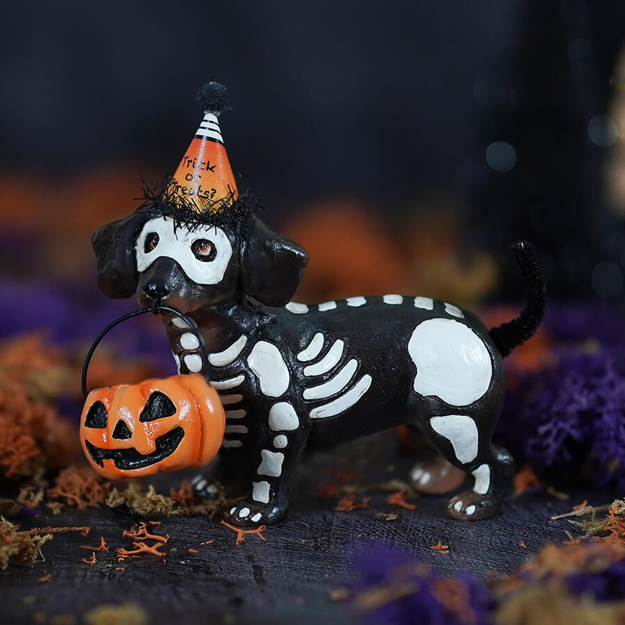 Black and white skeleton pup table piece dachshund figurine wearing orange party hat holding pumpkin basket