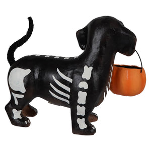 Black skeleton dachshund pup paper mache figurine with white bones holding an orange pumpkin bucket skelly pup paper