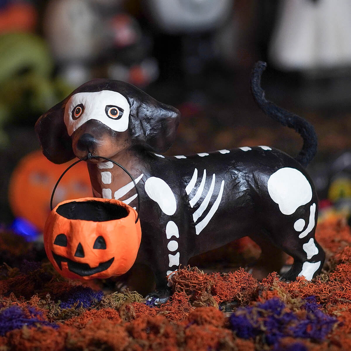 Black and white skeleton-themed dachshund skelly pup paper mache holding orange pumpkin treat bucket