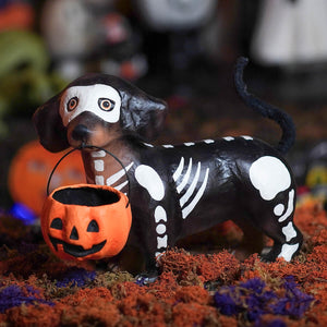 Black and white skeleton-themed dachshund skelly pup paper mache holding orange pumpkin treat bucket