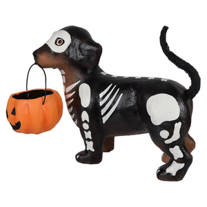 Black and white skeleton dachshund figurine holding orange pumpkin candy bucket in mouth skelly pup paper mache