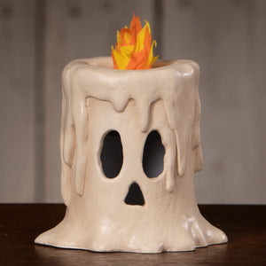 Cream-colored ceramic candle luminary with ghost face design and orange-yellow paper flame for spooky decor