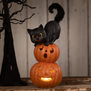 Small pumpkin stack black cat is a black plastic cat figurine on two glowing orange halloween pumpkins and gourds