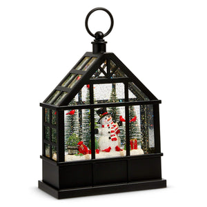Black metal lantern with glass interior featuring lighted decor of snowman red birds and miniature trees for holiday lights