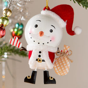 A cheerful white snowman ornament by bethany lowe design wearing a red santa hat holding mittens and a checkered sack