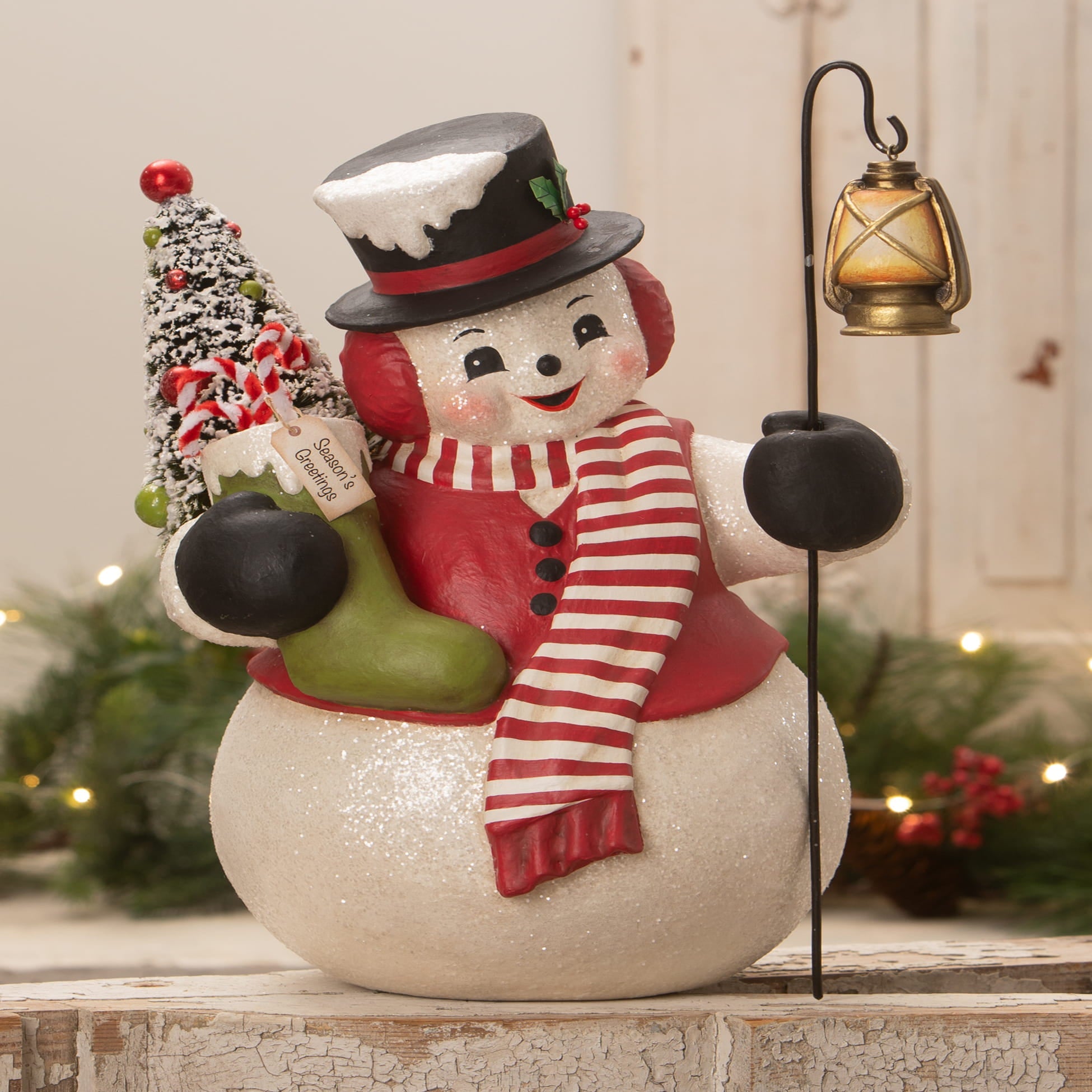 A cheerful snowman stanley figurine by bethany lowe designs wearing a red scarf holding a lantern and christmas tree
