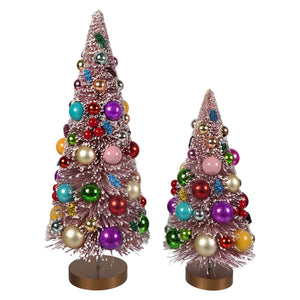 Two soft pink bottle brush trees decorated with colorful glass ornaments on bronze bases for holiday decor