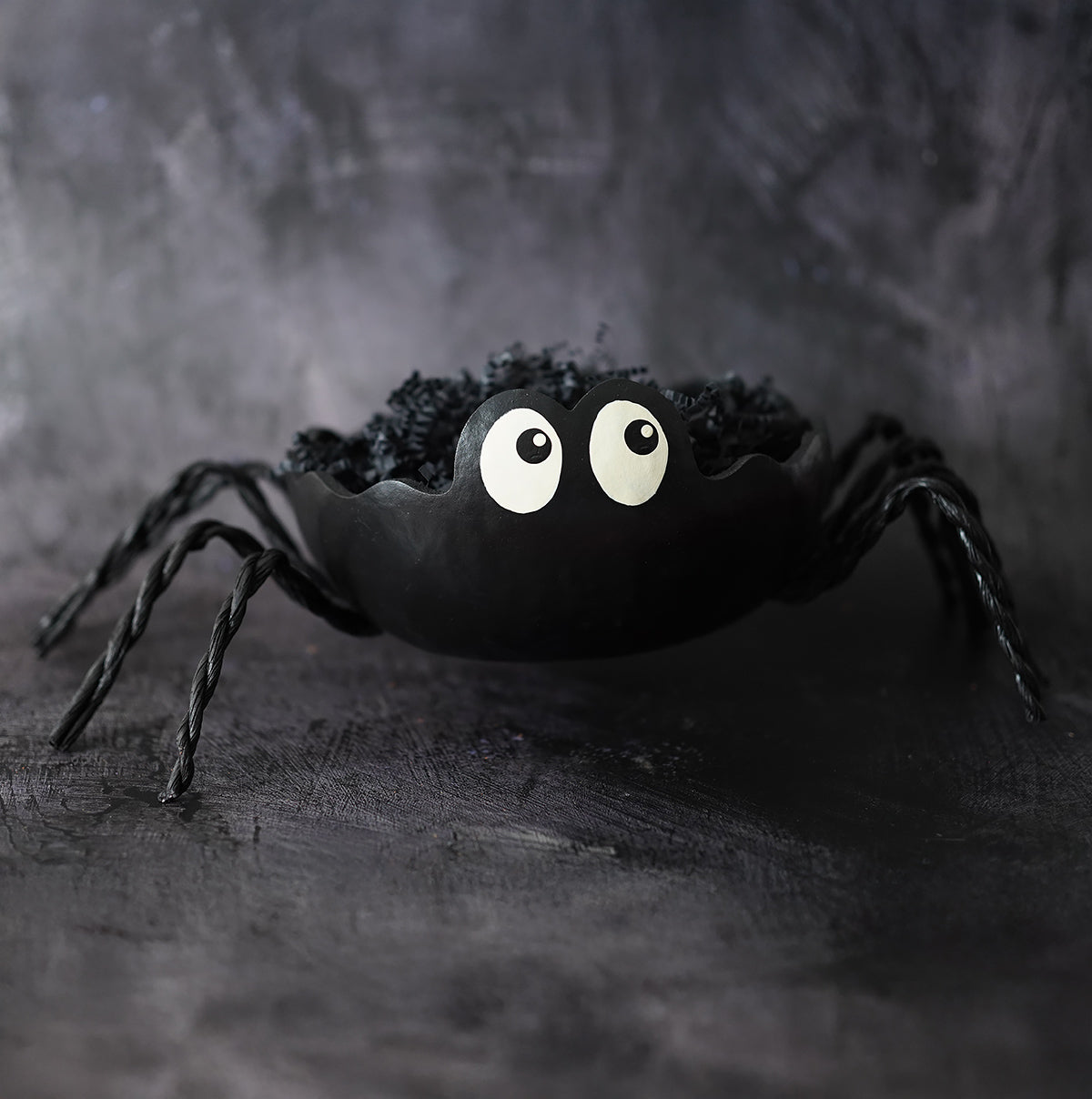 Black spider gourd candy dish with twisted legs oversized white eyes filled with dark shredded filler by meadowbrooke gourds artisans