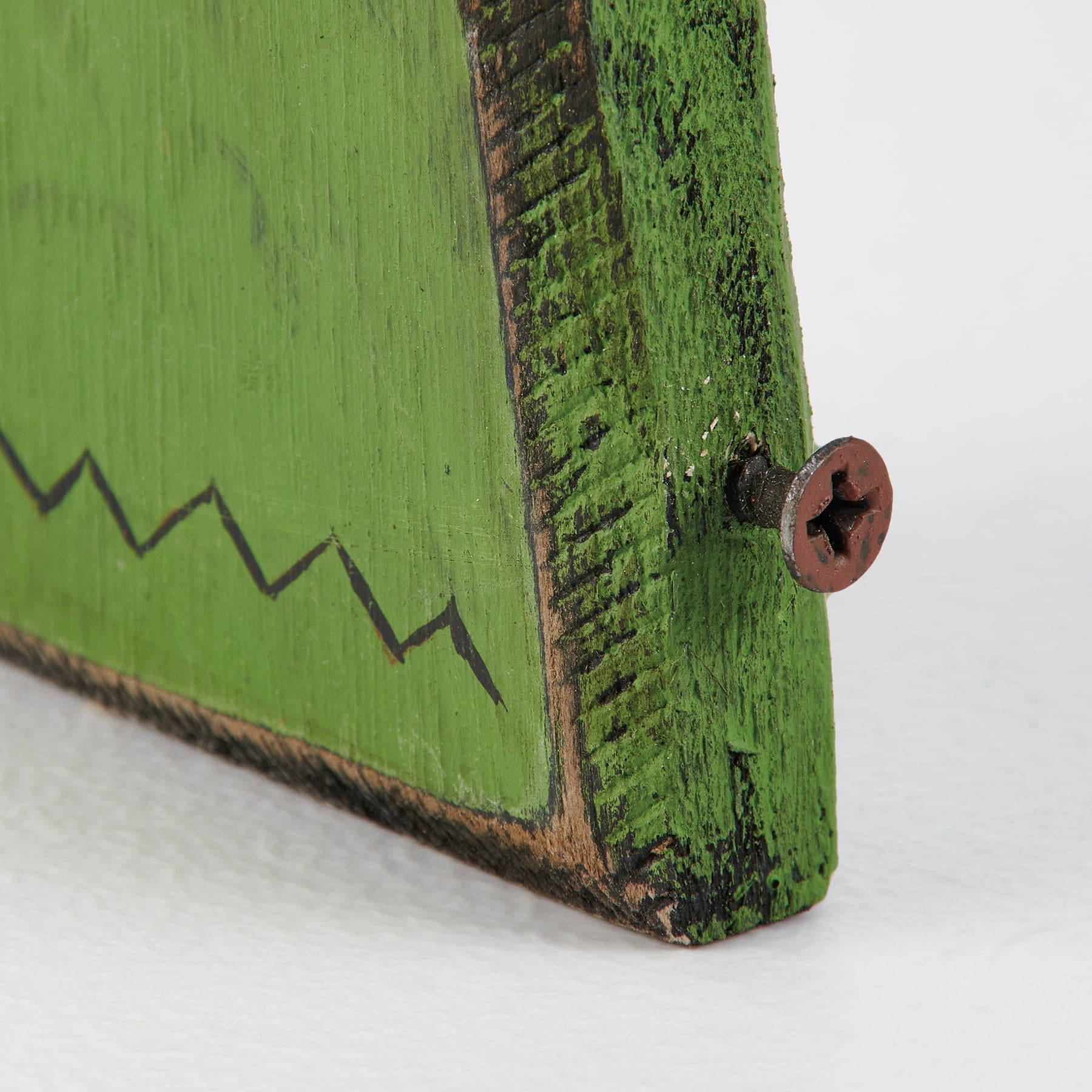 A rustic green wooden plaque with distressed finish and black zigzag detail from a vintage inspired spooky ornament set