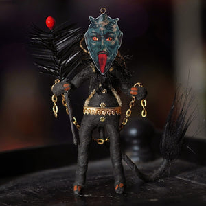 A spun cotton black krampus freestand ornament with a dark teal face, red eyes, black fabric, and gold chain details