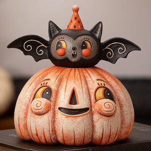 A whimsical squatty pumpkin batty figurine with a black bat in an orange polka-dot hat on a smiling halloween pumpkin