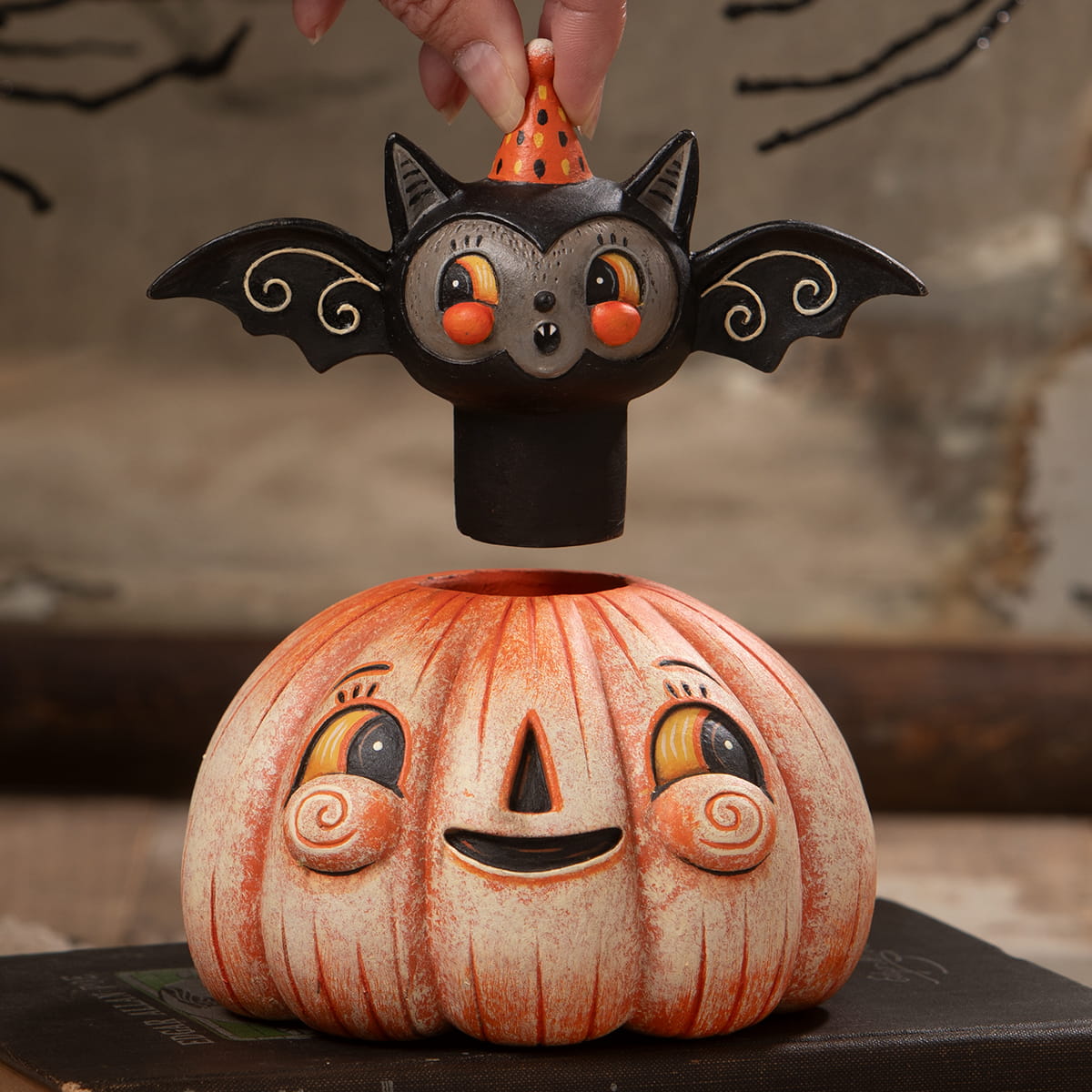 Orange and white ceramic halloween pumpkin with black bat figurine wearing orange polka dot hat on top