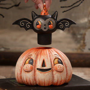 Orange and white ceramic halloween pumpkin with black bat figurine wearing orange polka dot hat on top