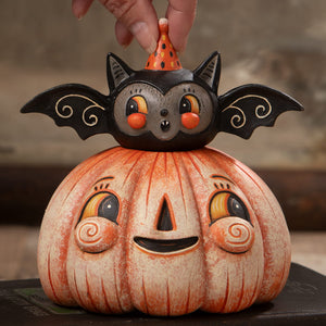 A charming halloween pumpkins and gourds ceramic figurine with a smiling orange pumpkin and a black bat wearing a party hat