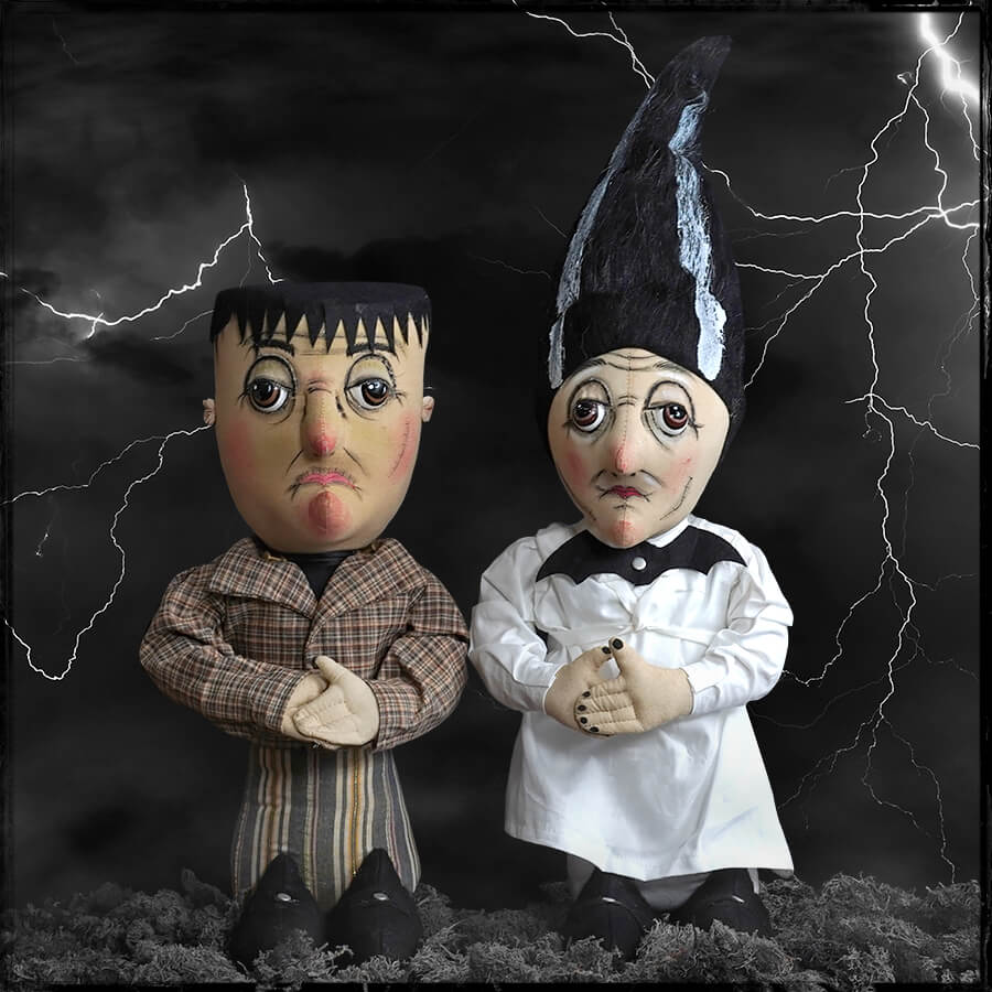 Two handcrafted carlos stein joe spencer halloween dolls depicting frankenstein and bride stand against stormy backdrop