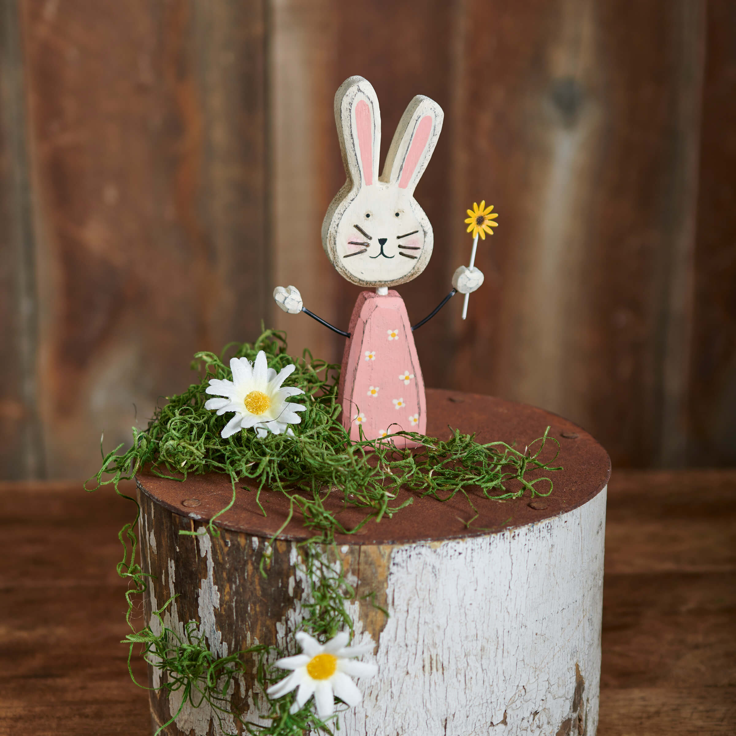 A charming wooden sunny bunny chunky sitter in a pink dress with yellow flowers holding a small yellow flower