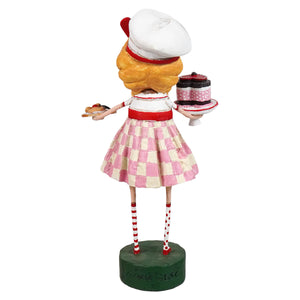 A lori mitchell figurine of a blonde waitress in a pink and white checkered skirt holding a tray with valentine treats cake