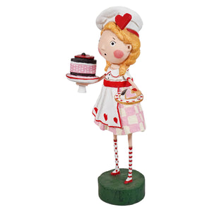 A lori mitchell figurine of a blonde young chef in white and pink holding valentine treats spreading holiday cheer