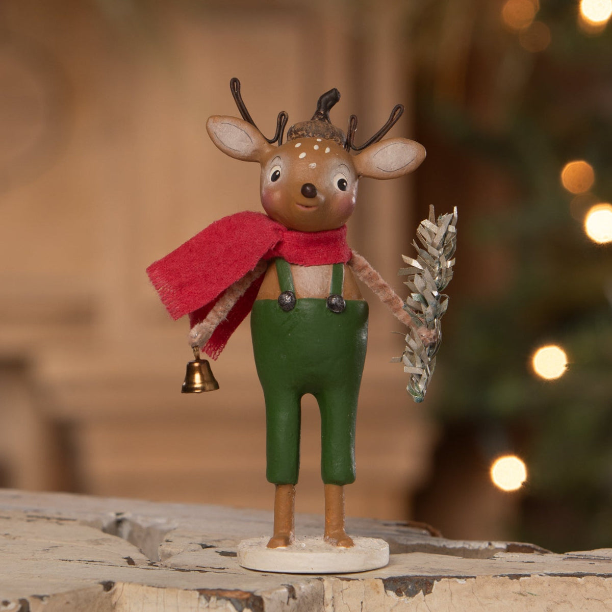 A sweet reindeer wooden figurine by bethany lowe designs wearing green overalls and holding a silver wreath and bell