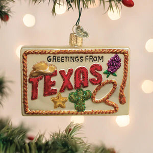 A festive glass texas postcard ornament shaped like a license plate with glittery red lettering and texas-themed decorations