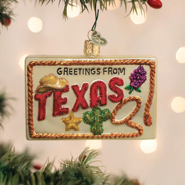 A festive glass texas postcard ornament shaped like a license plate with glittery red lettering and texas-themed decorations