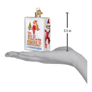 A clear glass book-shaped elf on the shelf ornament with red-clad elves perfect for world christmas decor