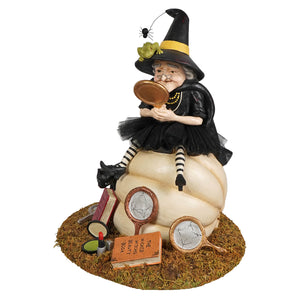 A whimsical fairest witch figurine by bethany lowe designs in black hat and dress on a cream pumpkin base with decor items