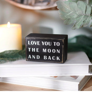Black wooden box sign with white lettering love you to the moon and back featuring round trip theme