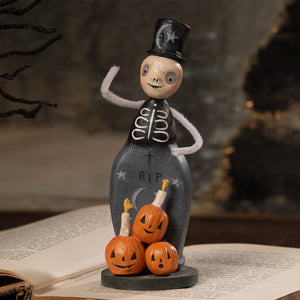 A whimsical halloween figural decor trickster skeleton in a dark gray coffin outfit with top hat and jack-o-lanterns