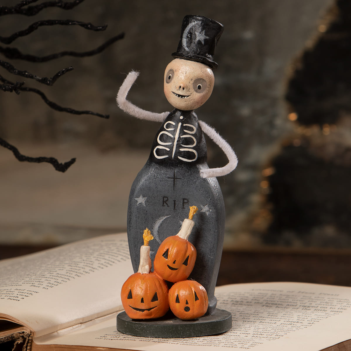 A whimsical skeleton trickster figurine in black top hat and vest with three orange jack-o-lanterns halloween figural decor