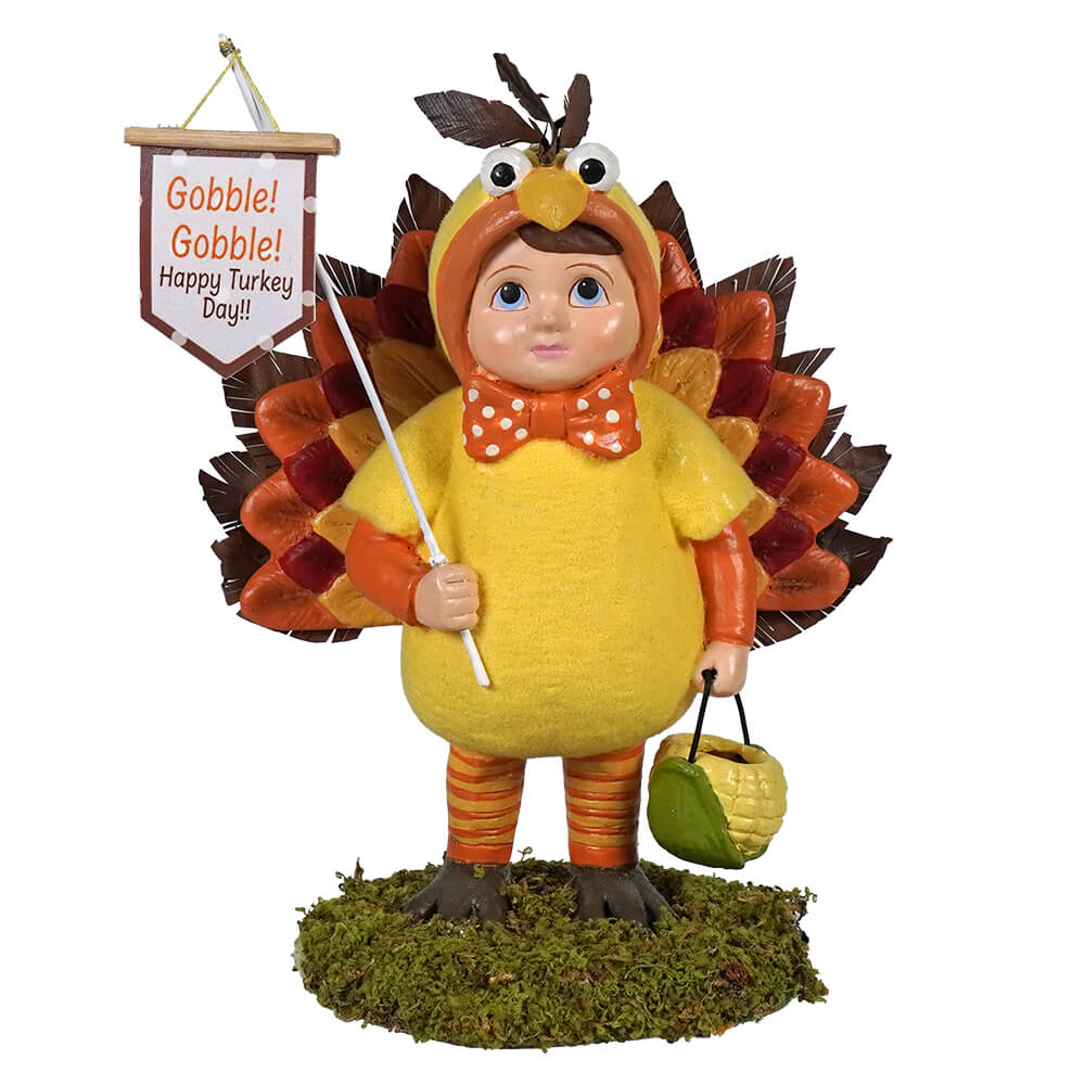 A yellow tommy turkey boy figurine by bethany lowe design with orange brown feathered wings holding a gobble sign made of pressed paper