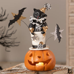 Black cat figurine with gold party hat and white collar standing on a carved orange jack o lantern pumpkin
