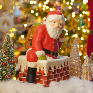 Traditional santa down chimney large paper mache figurine in red and white with black belt sitting on snowy brick chimney