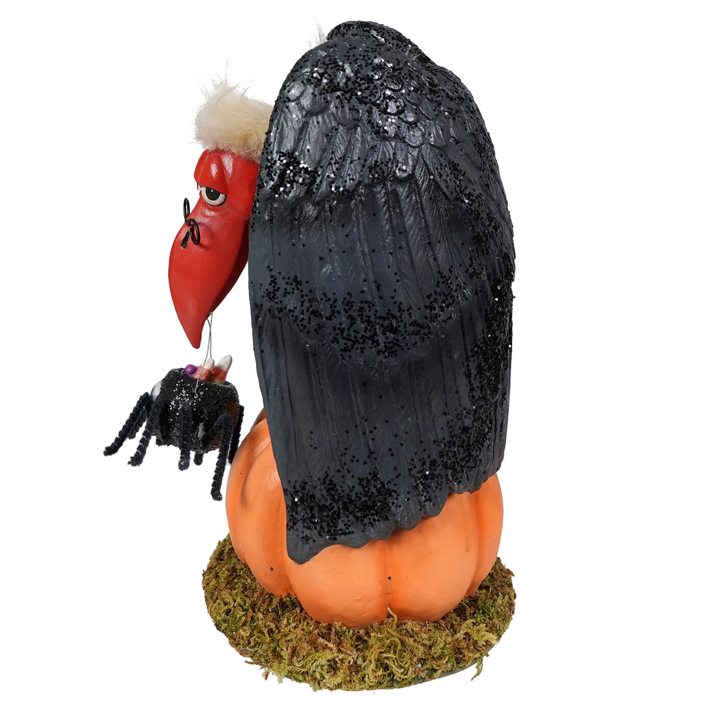 A black glittery vulture figurine with a red beak and white tufted head perched on an orange pumpkin base treats for the buzzard