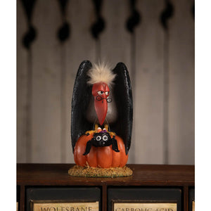 A whimsical black vulture figurine with white feathered crest and red beak perched on an orange pumpkin with a black spider in treats for the buzzard