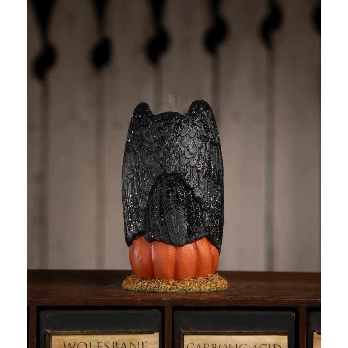 Black owl figurine with detailed feather texture perched on an orange pumpkin base for treats for the buzzard
