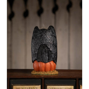 Black owl figurine with detailed feather texture perched on an orange pumpkin base for treats for the buzzard